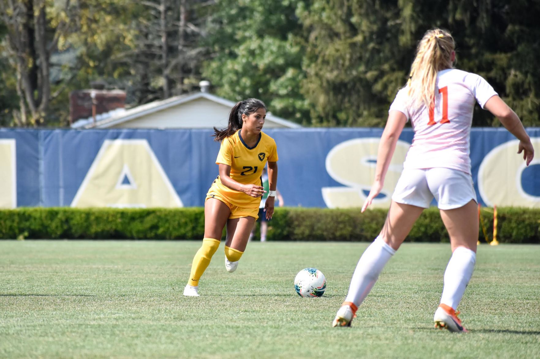 A WVU women's soccer player dribbles the ball down the field.